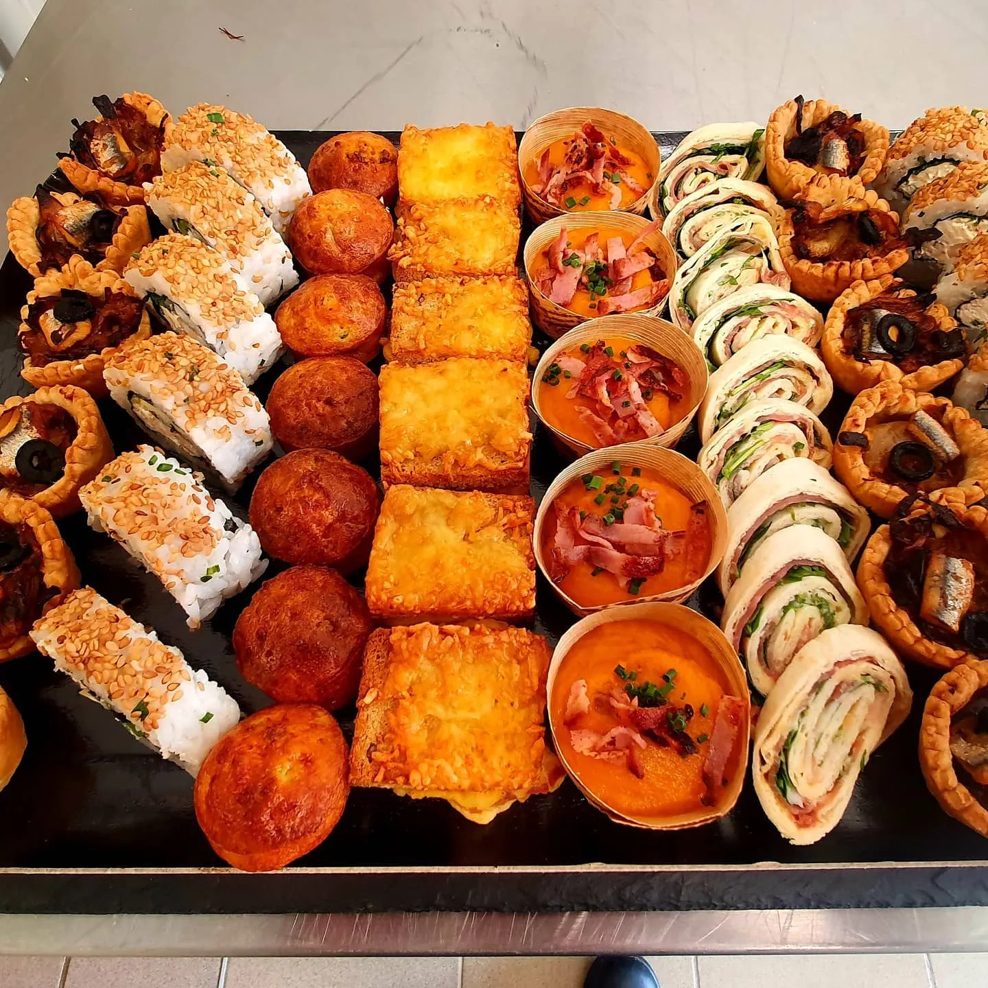 Plateau de bouchées salées alignées par rangées, makis, petits muffins, toasts gratinés, verrines et wraps roulés